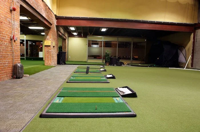 Indoor golf driving range with multiple hitting mats and a large window at the back.