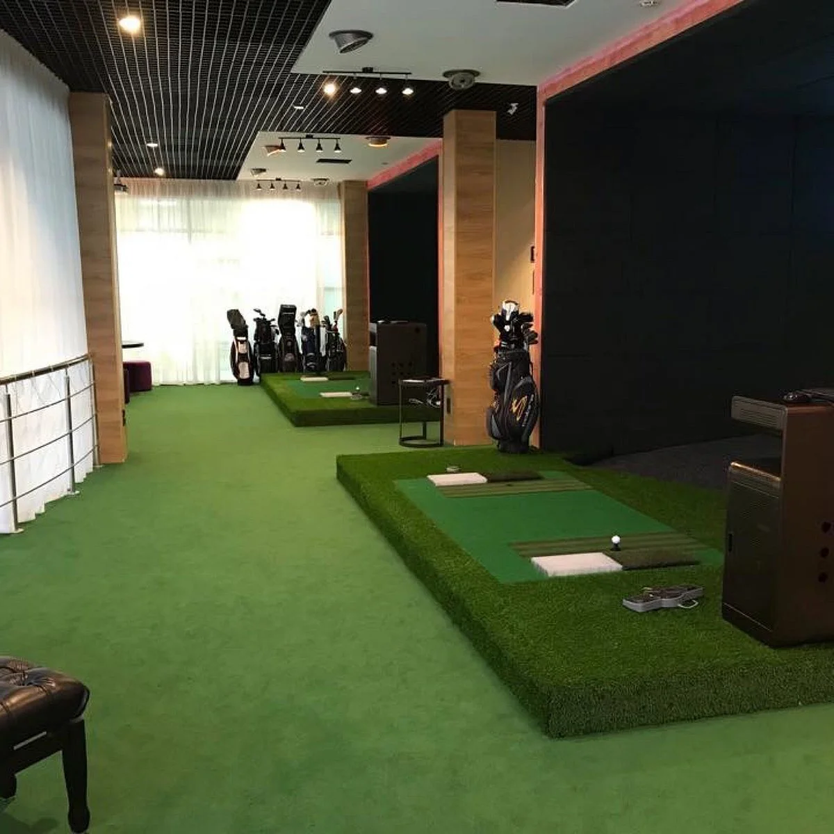 Indoor golf practice area with artificial green turf, golf clubs in bags, and three golf hitting stations.