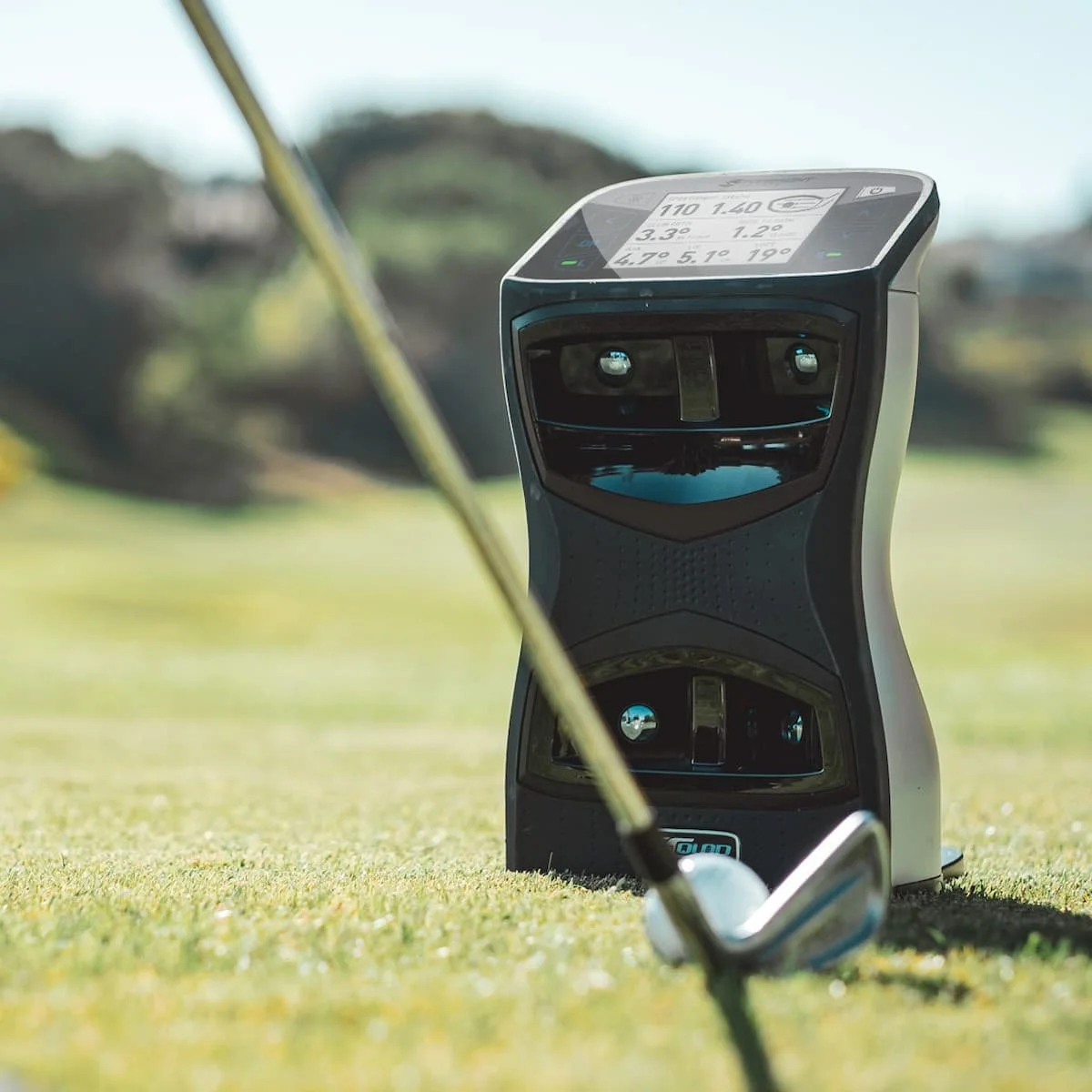 Golf rangefinder on a grassy golf course with golf club in foreground.