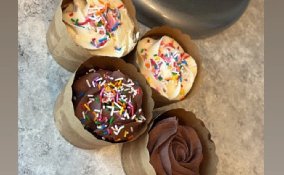 Four cupcakes with different frosting and sprinkles, placed inside paper cupcake holders on a countertop.