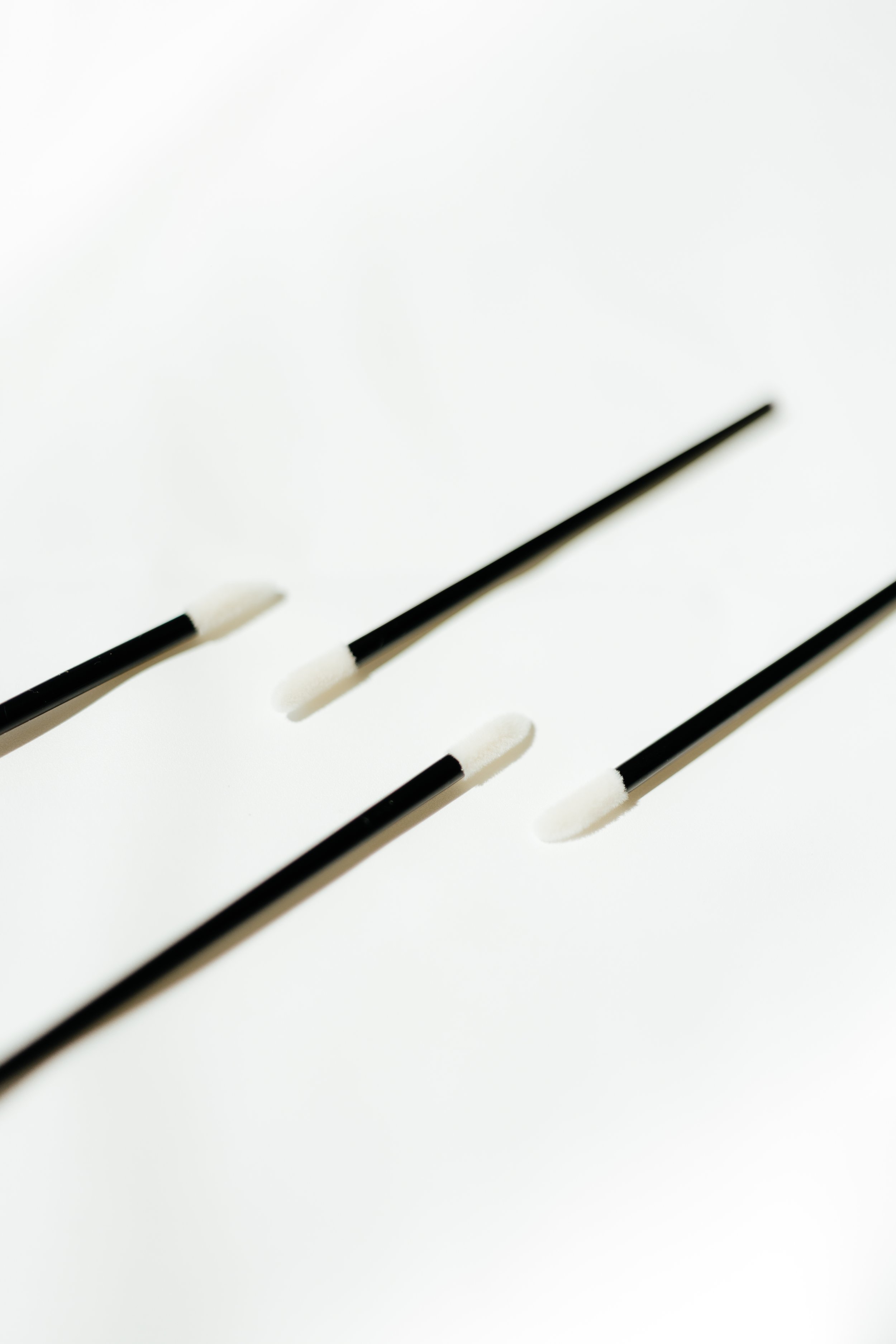 Four black makeup applicator wands with white sponge tips on a white background.