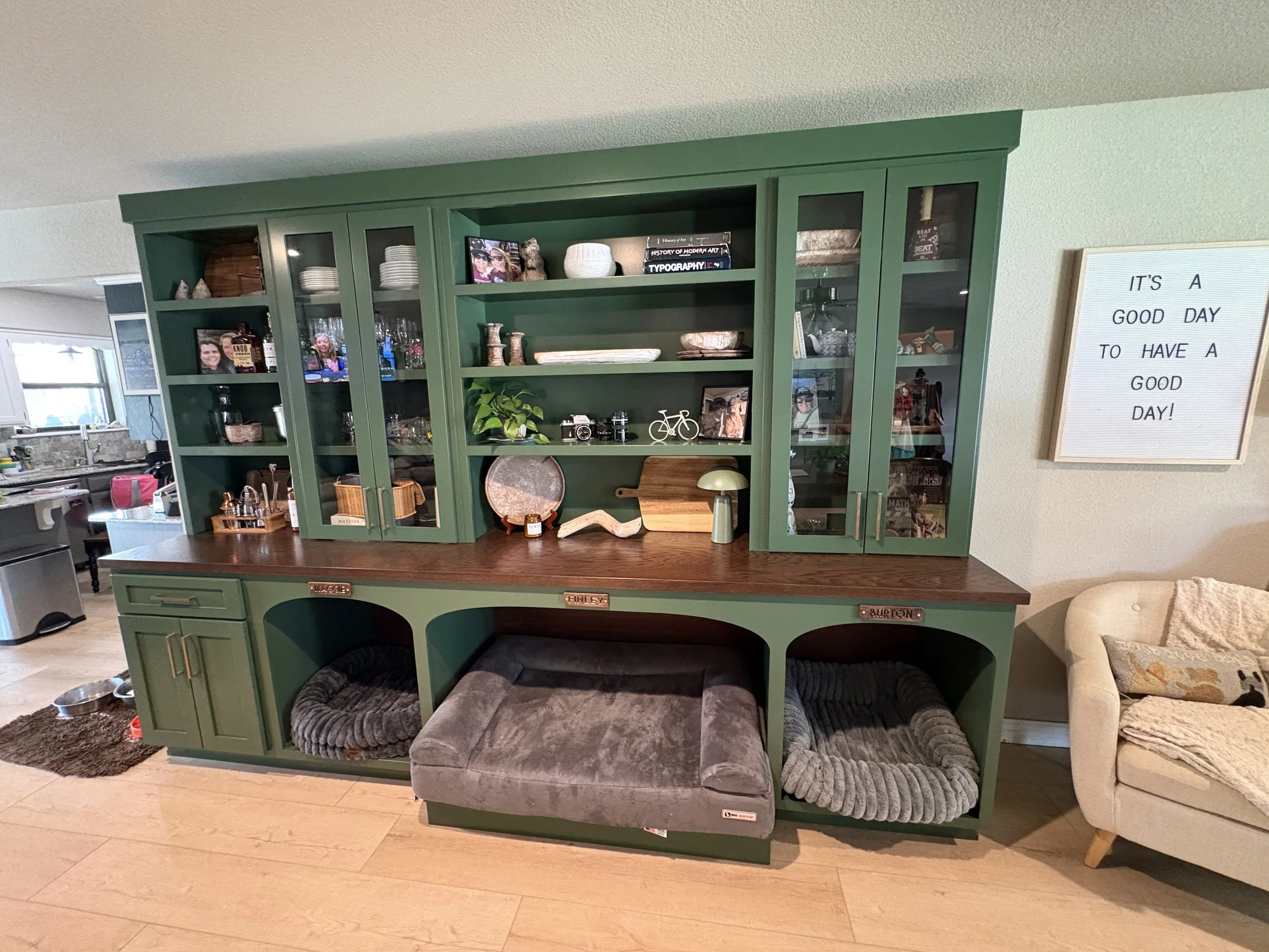 Dog beds built into green bookshelf cabinets with glass doors and a wood counter top.