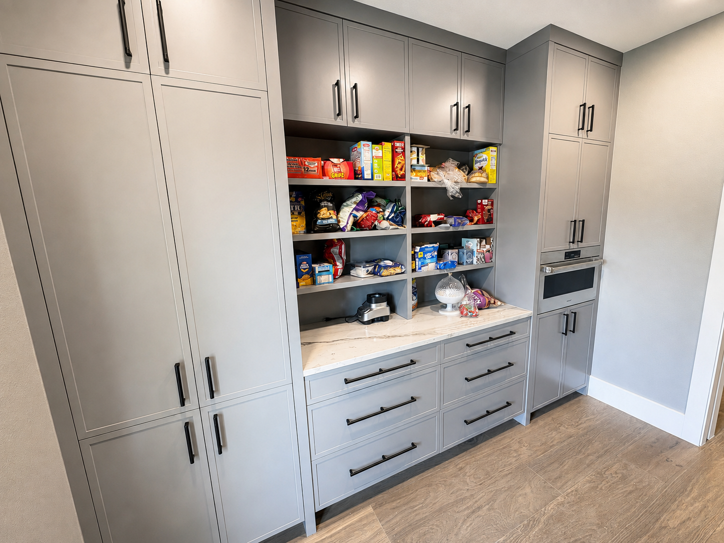 Grey butler pantry cabinets with a tall cabinet and open shelving in the middle with food items on it.