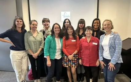 Group of ten women smiling and standing together in a room for a photo.