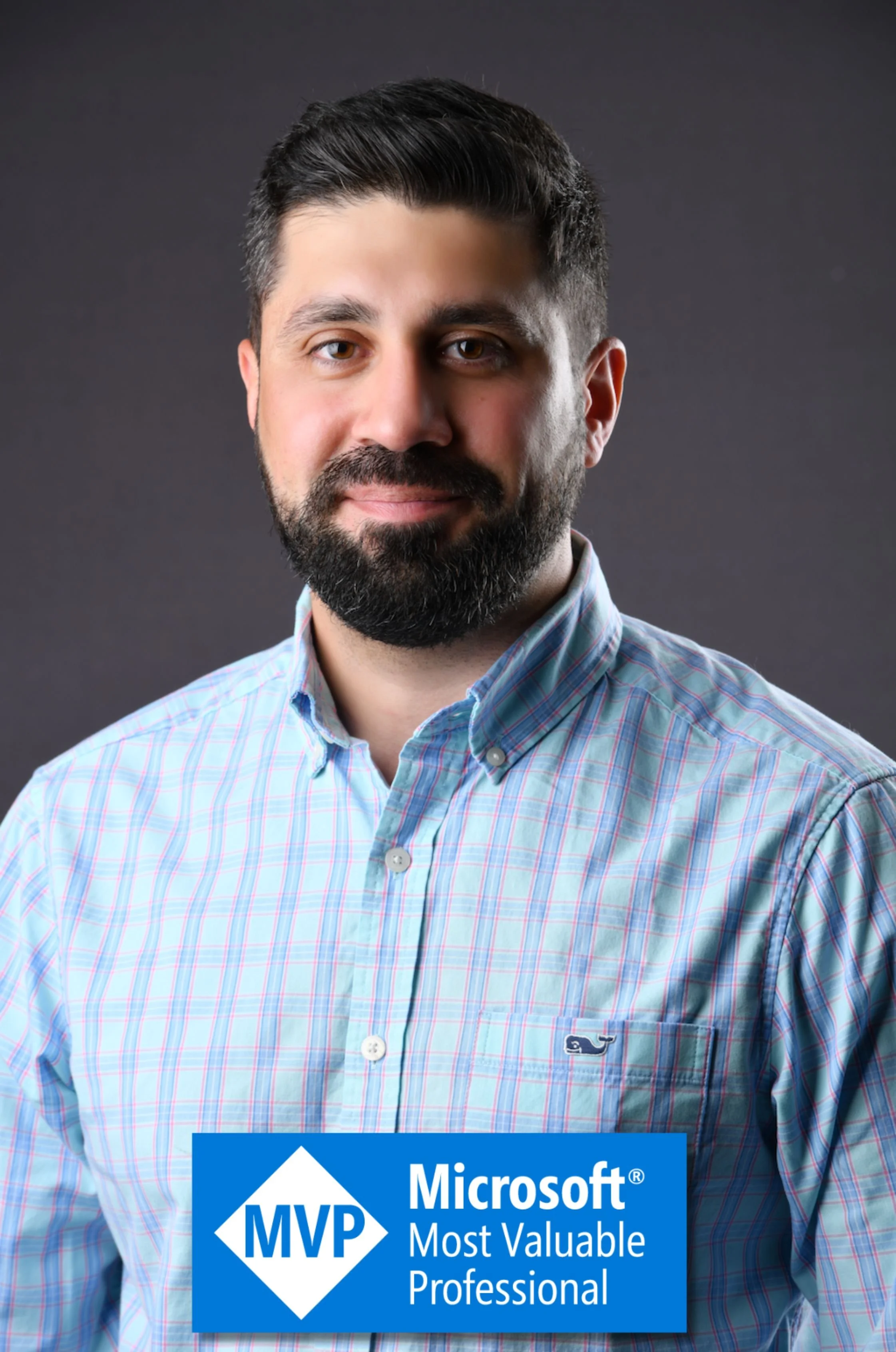 Headshot of a man with dark hair and beard, wearing a plaid shirt, against a dark background, with a blue badge reading "MVP Microsoft Most Valuable Professional" at the bottom.