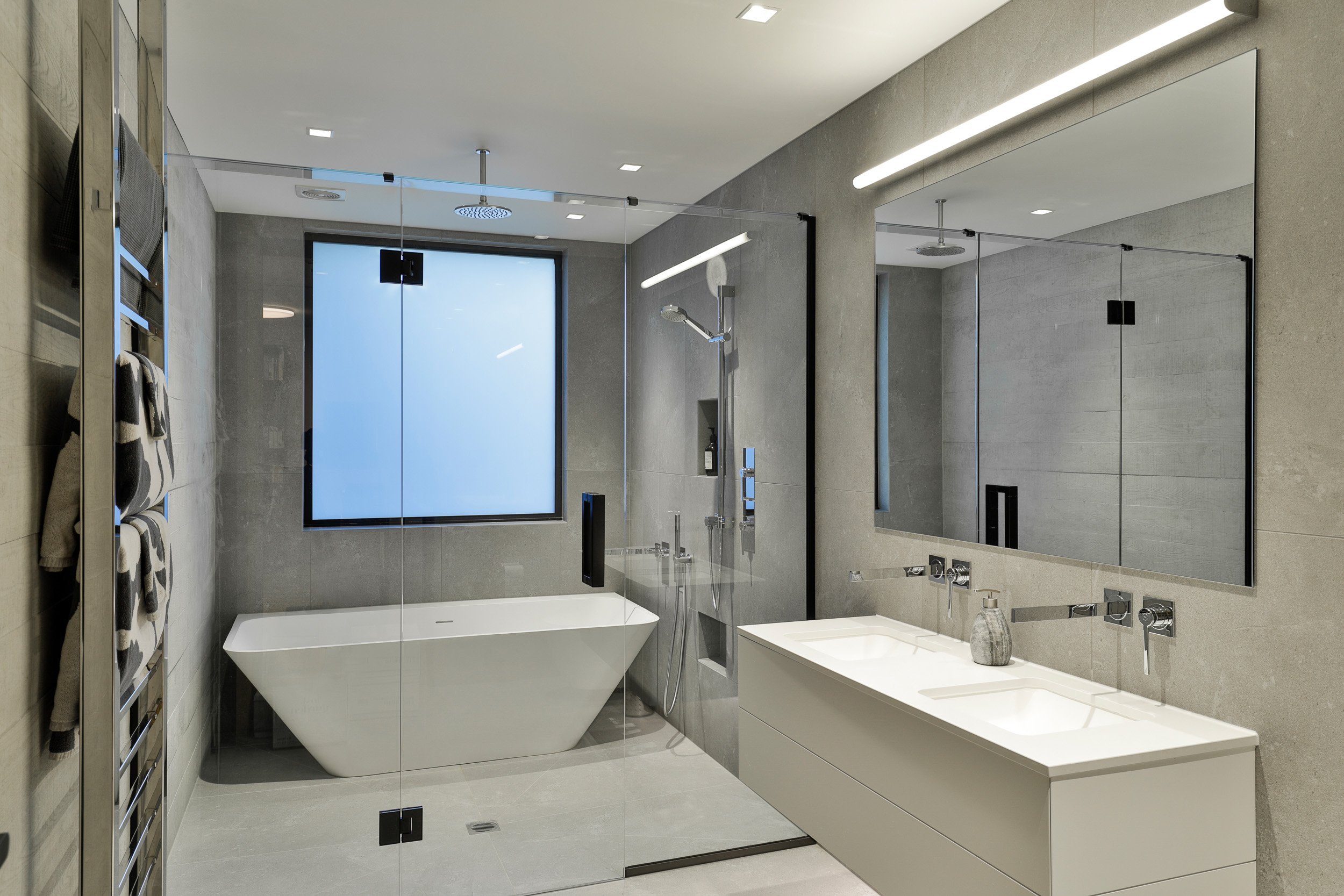 Modern bathroom featuring a freestanding bathtub, double vanity with sinks, glass shower enclosure, and sleek gray walls.