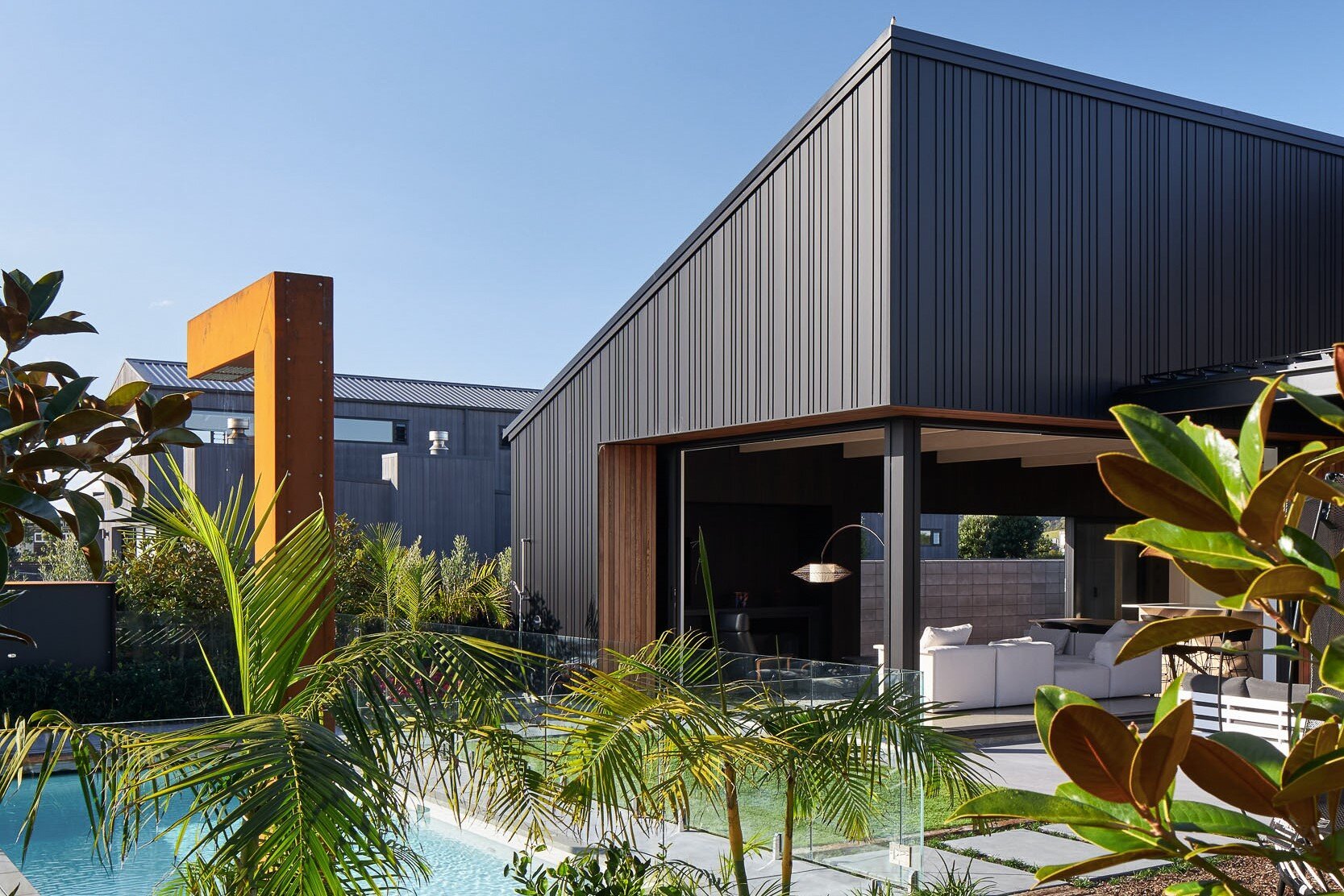 Modern home with a unique design, surrounded by lush greenery and a pool, showcasing a blend of wood and metal elements.