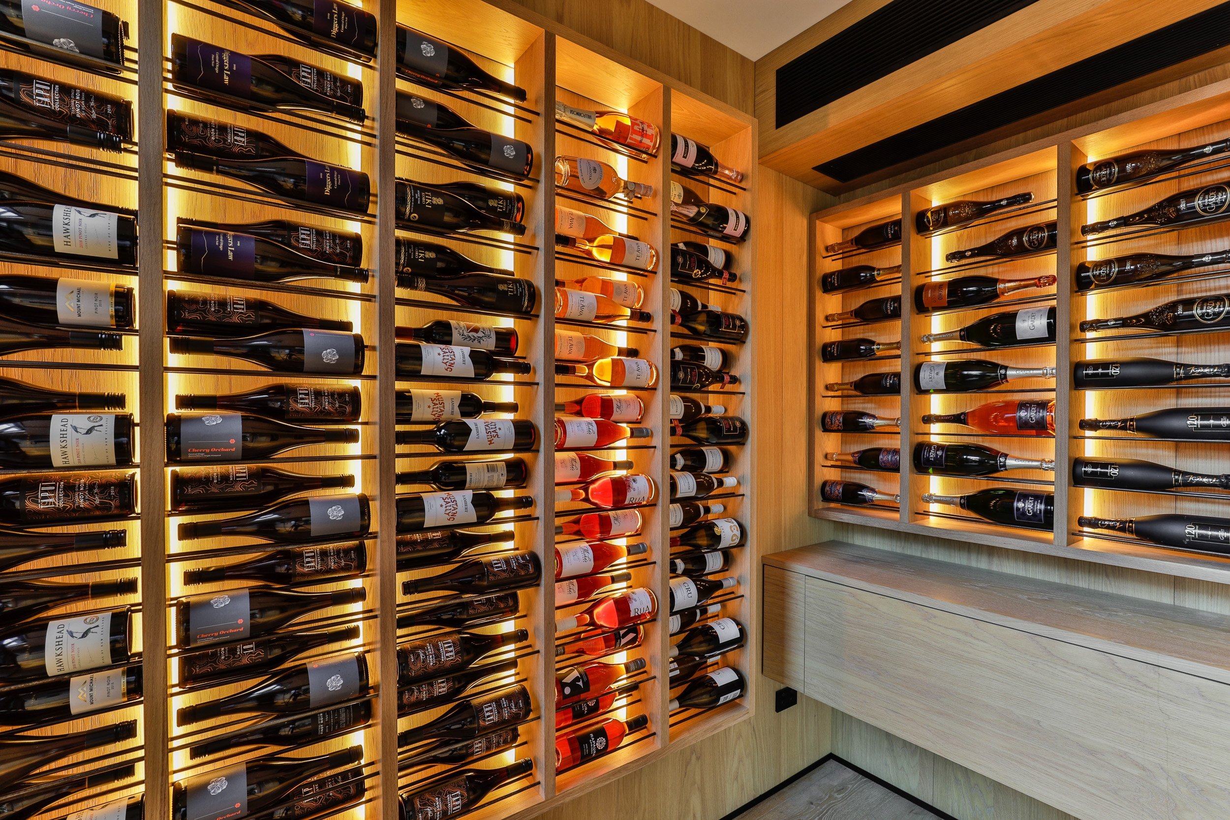 A stylish wine cellar featuring illuminated wooden shelves filled with various wine bottles, showcasing an elegant wine collection.
