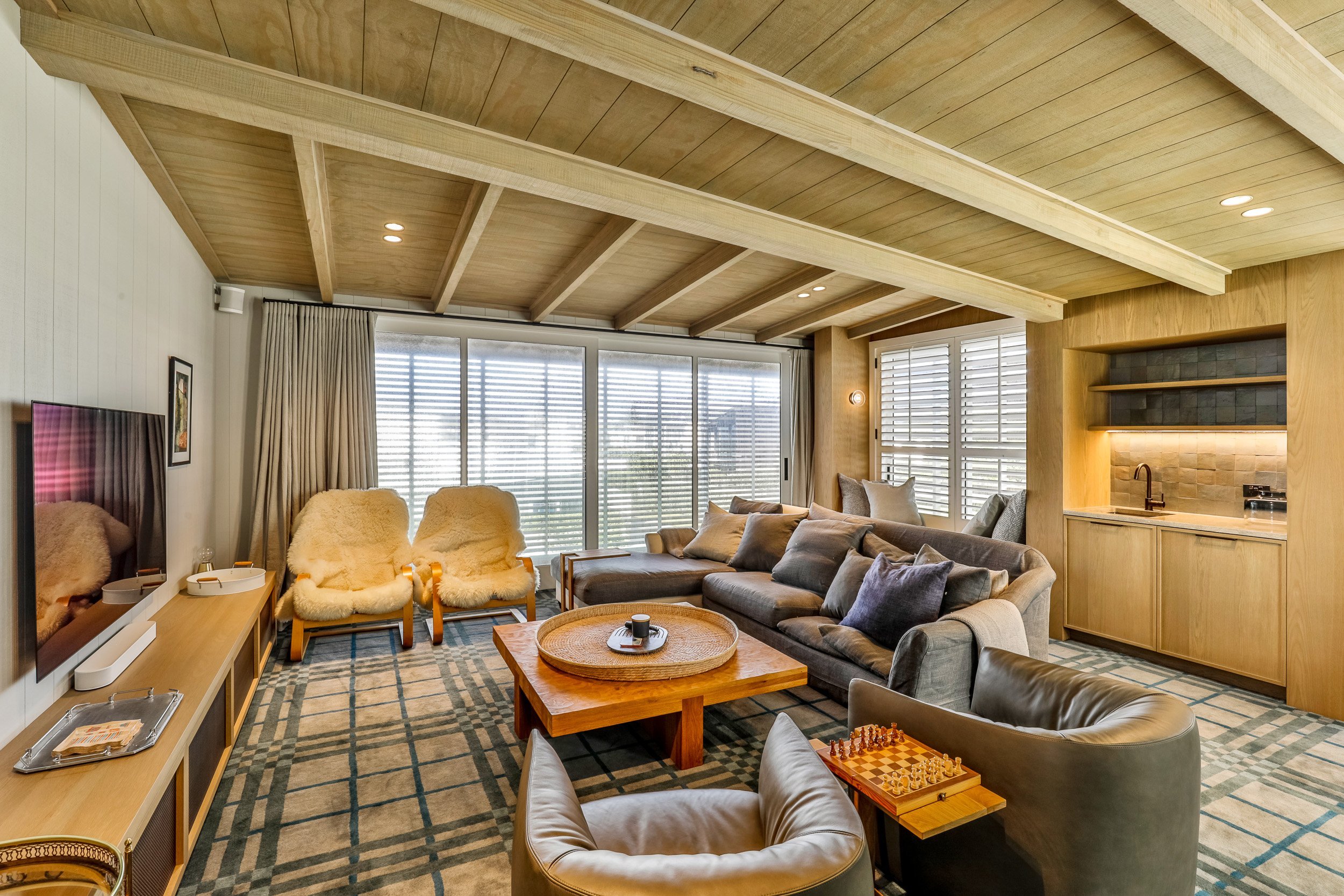 Cozy living room with wooden beams, plush seating, a chess set, and large windows allowing natural light to fill the space.