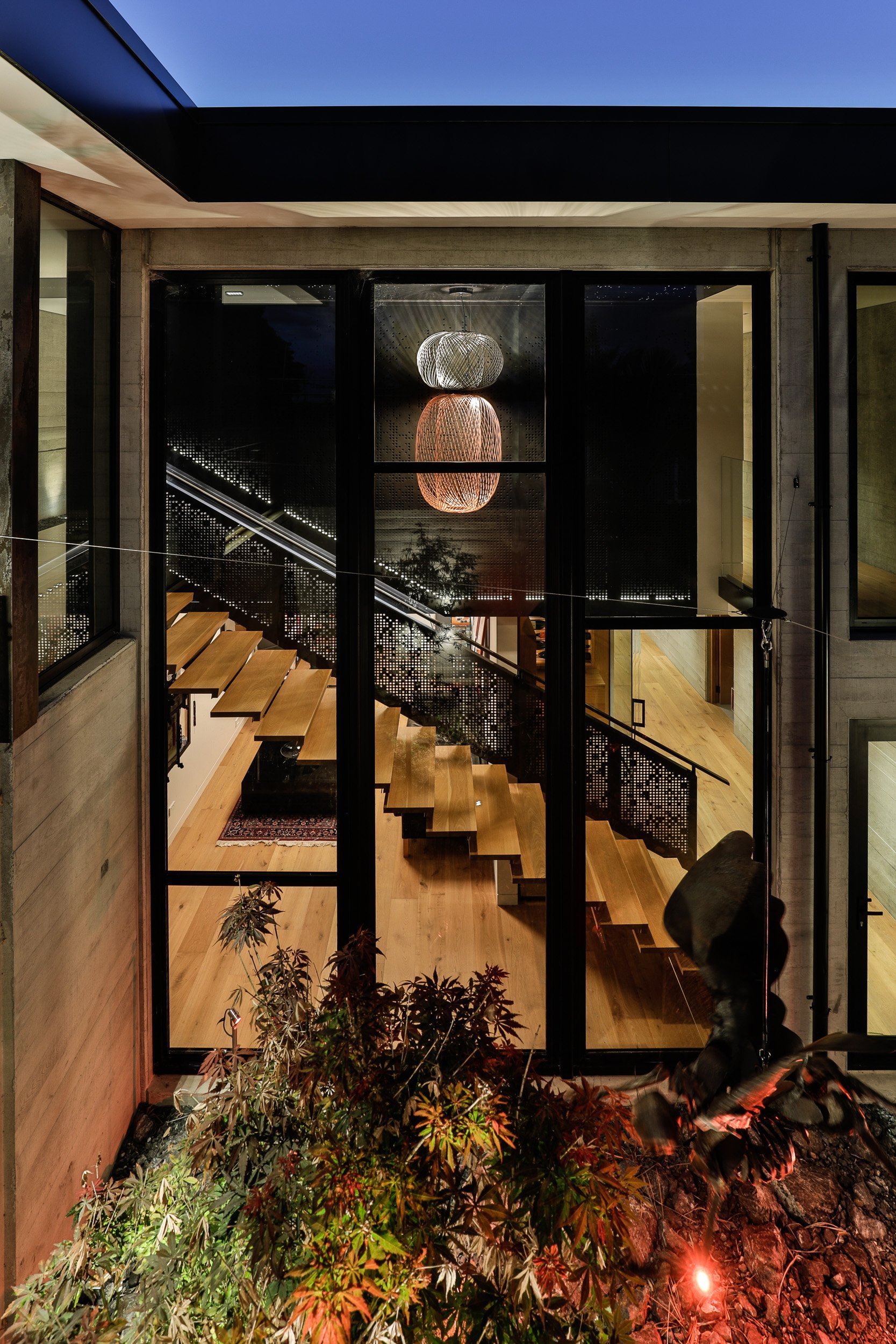 A modern stairway illuminated by a stylish pendant light, framed by large glass doors with a garden visible outside at dusk.