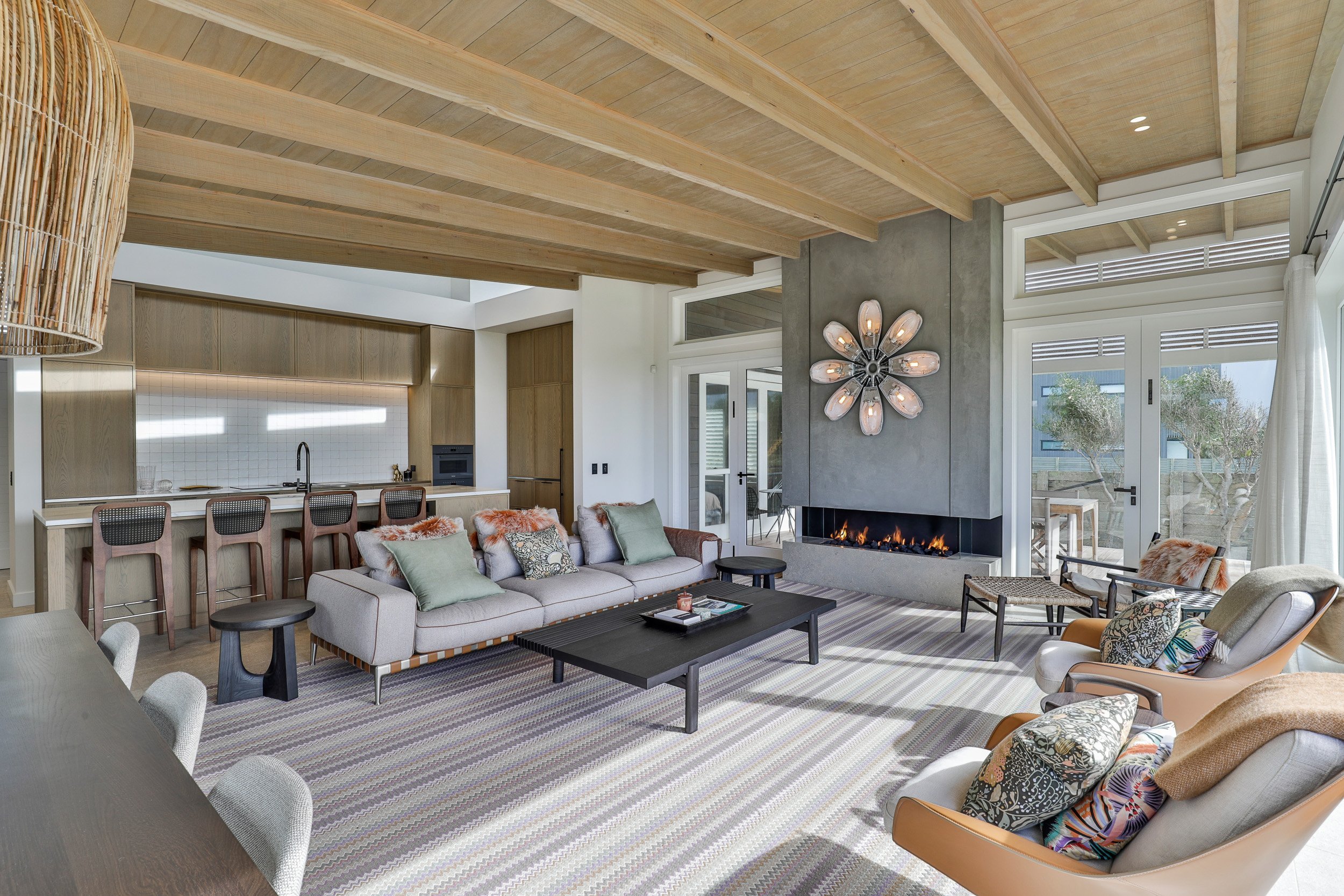Modern living room featuring a gray fireplace, artistic light fixture, cozy sofa, and a view of greenery through glass doors.
