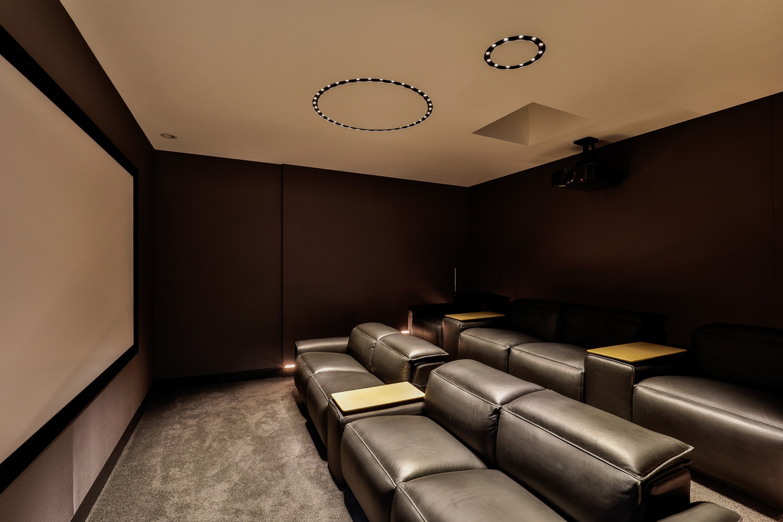 A luxurious home theater featuring dark leather seating, subdued lighting, and a large screen for an immersive viewing experience.