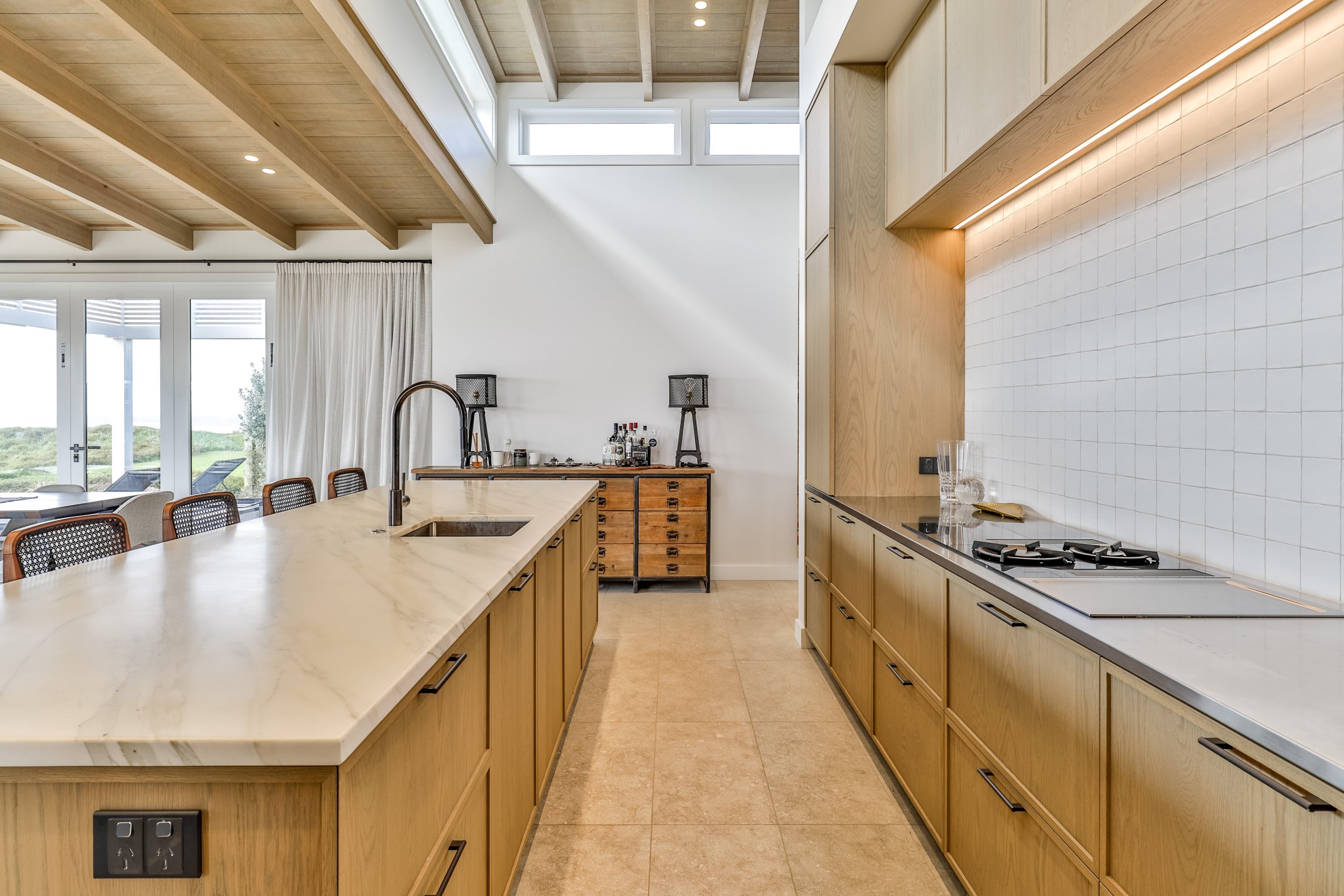 Modern kitchen featuring light wood cabinetry, a marble island, and stylish wooden stools with mesh backs, illuminated by soft lighting.