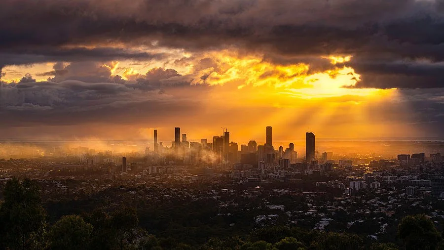 Sunset over a city skyline with dark clouds and a vibrant yellow and orange sky.