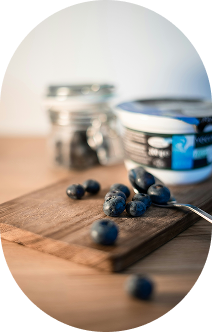 Fresh blueberries on a wooden cutting board with a container and a spoon nearby.