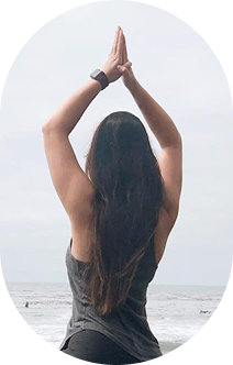 Woman practicing yoga on the beach with hands raised in prayer position facing the sky