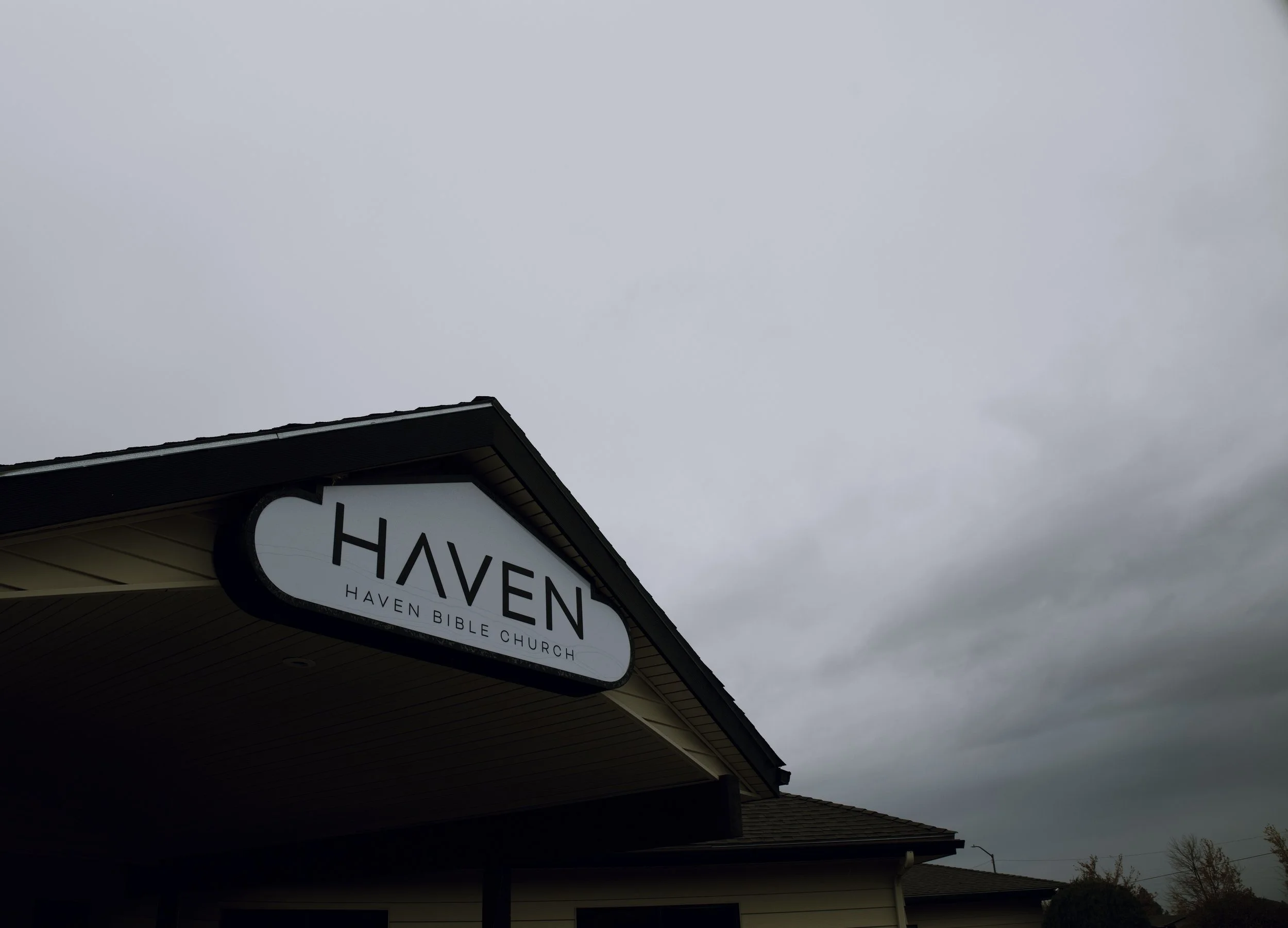 Sign for Haven Bible Church on the side of a building with a cloudy sky in the background.