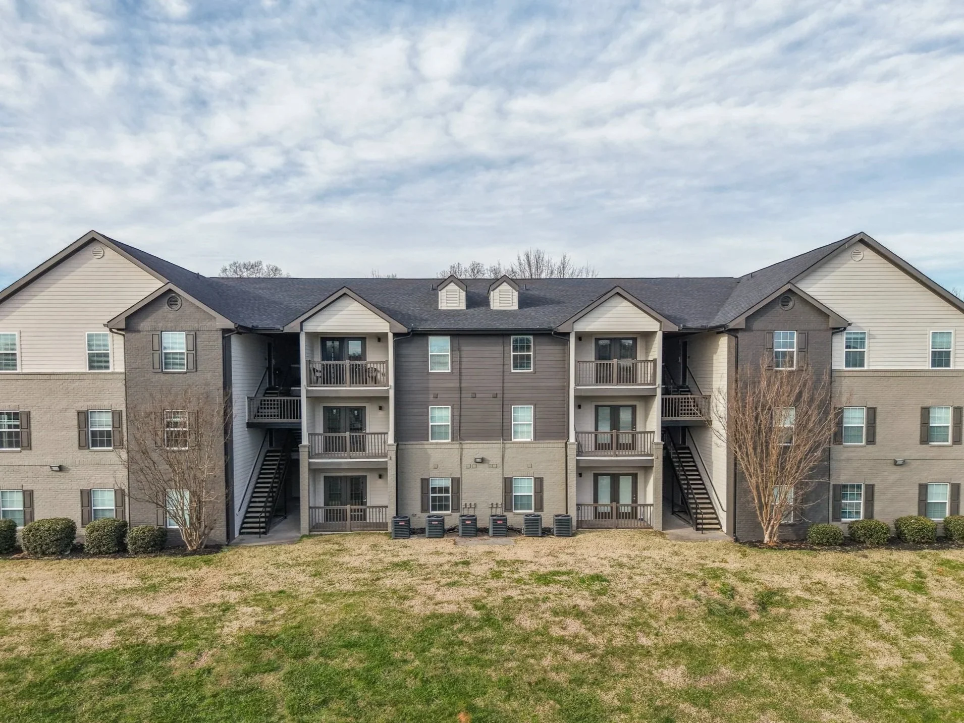 Multi-story residential apartment buildings on a grassy slope under a partly cloudy blue sky.