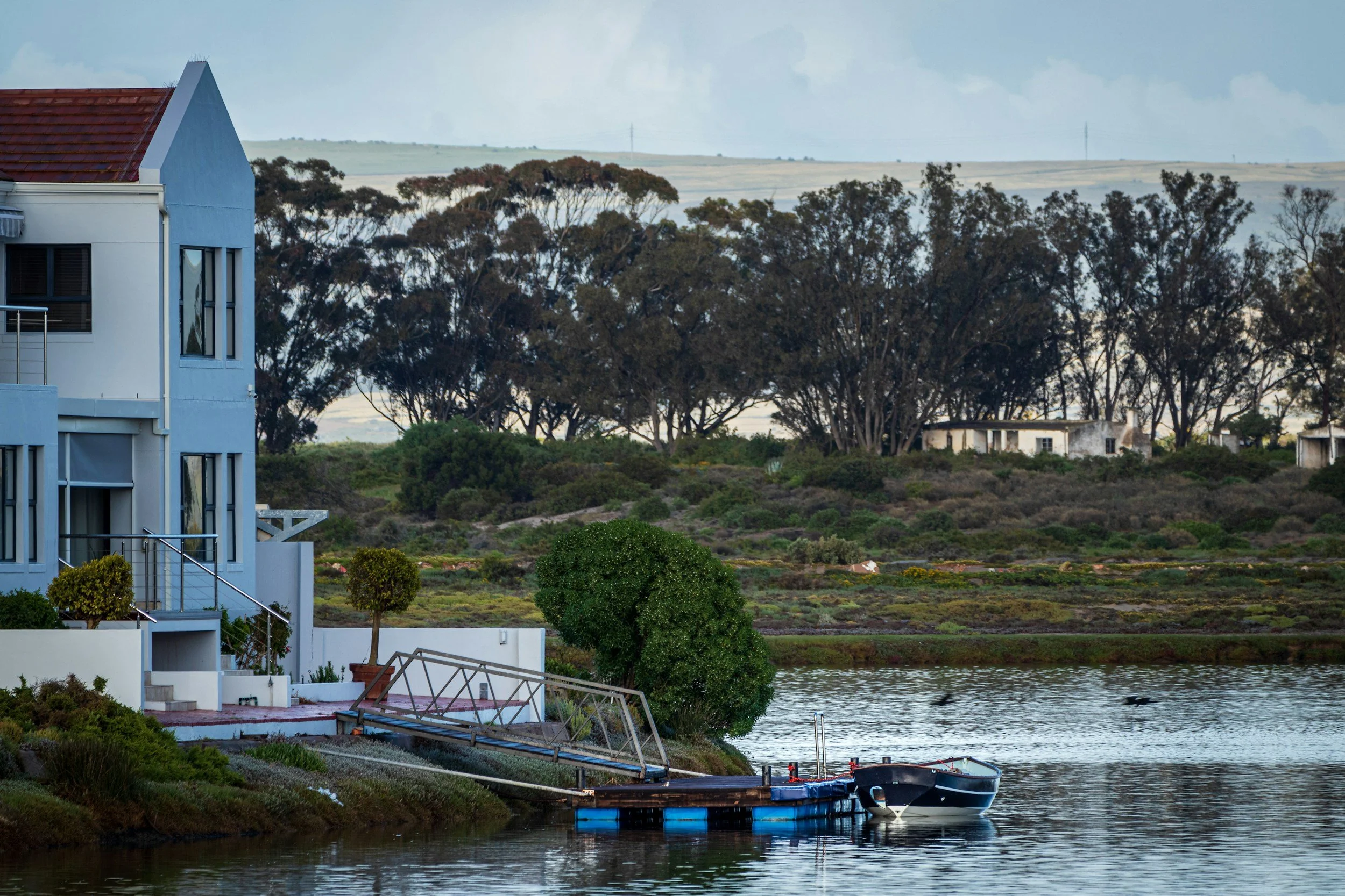 White 2 story house with boat dock showing the water it is on with boat tied to the dock.