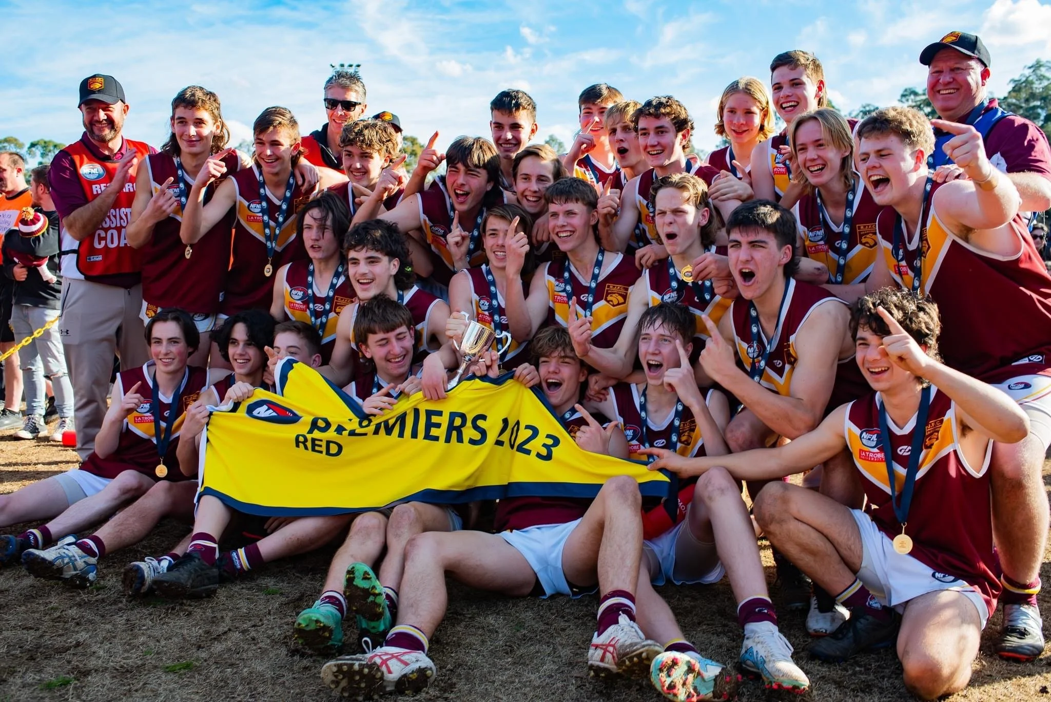 A group of young football players and coaches celebrating with medals and a trophy after winning a game or championship.