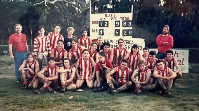 Group of young soccer players and two adults pose for a photo on a grassy field, wearing red and white striped jerseys