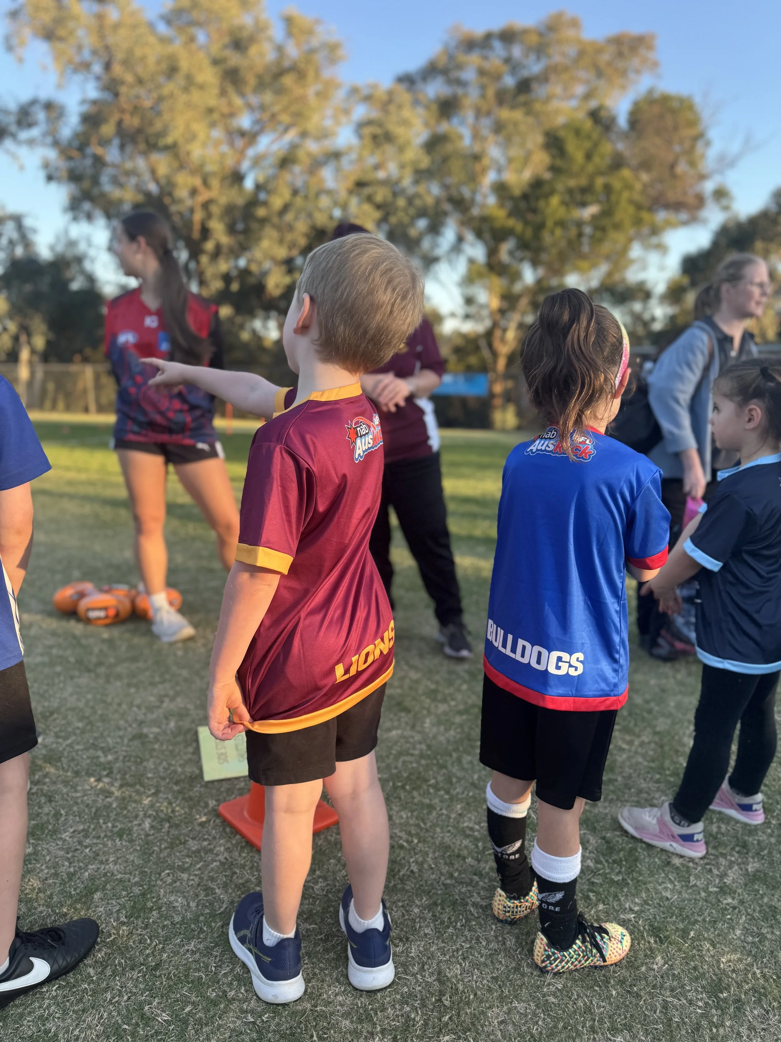 Kids wearing sports jerseys at a sports field during late afternoon.