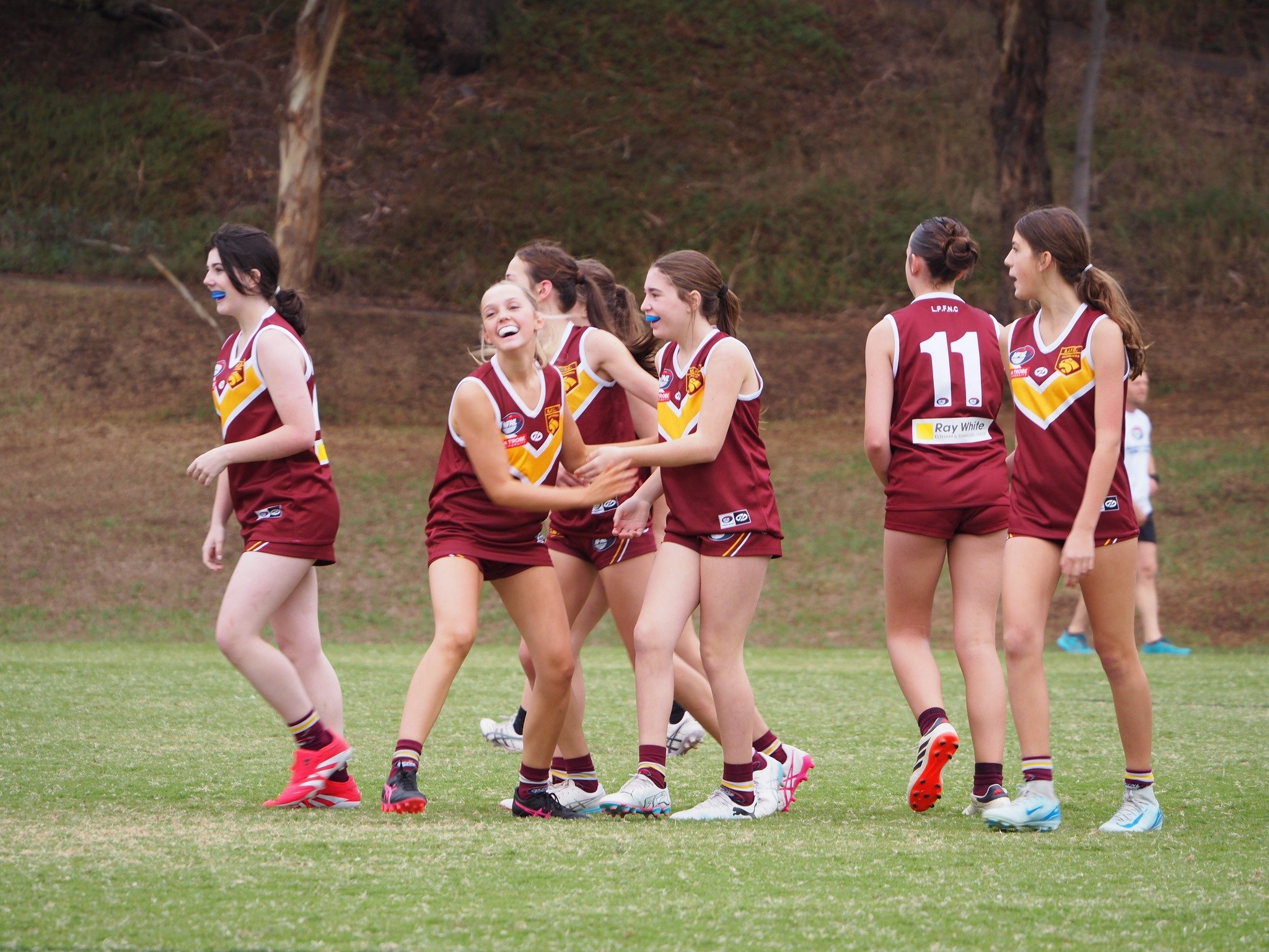 A group of female Australian rules football players in maroon and yellow uniforms celebrating on the field.