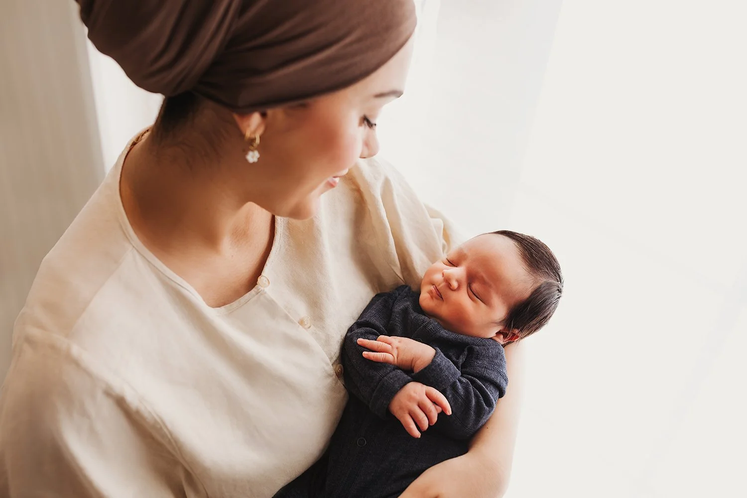 En mor holder sin sovende baby i armene i et lyst og luftig rom.