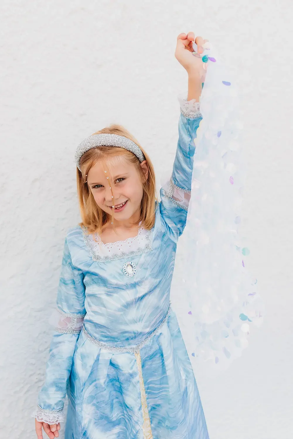 En jente som smiler mens hun viser frem den blå prinsessekjolen hennes.
