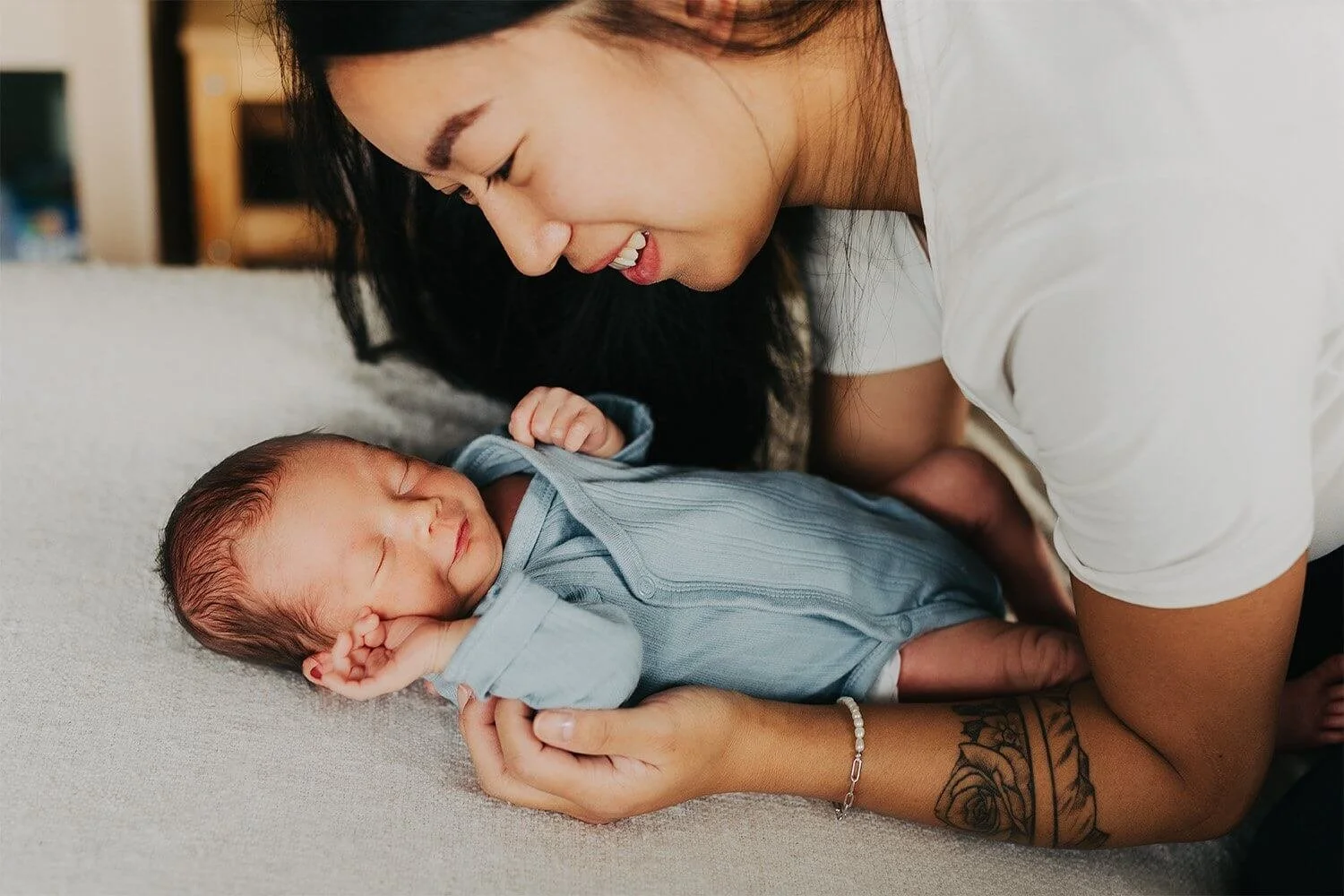 Nyfødtfotografering hjemme i Drammen: En smilende mor ser ned på sin sovende baby i en blå body.