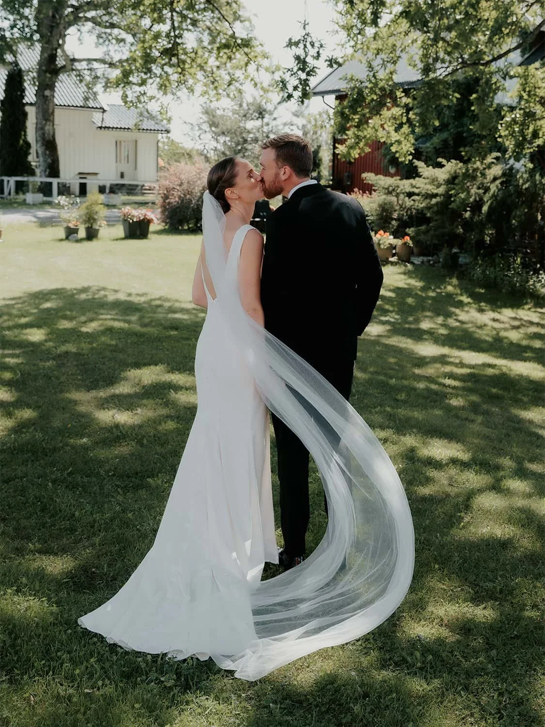 Brudepar kysser ute på gressplen under bryllupsfotografering på Grønsand Gjestegård.