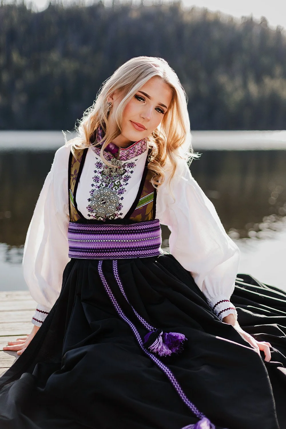 En konfirmant i tradisjonell bunad som sitter på en brygge ved vannkanten på Stordammen, Konnerud.