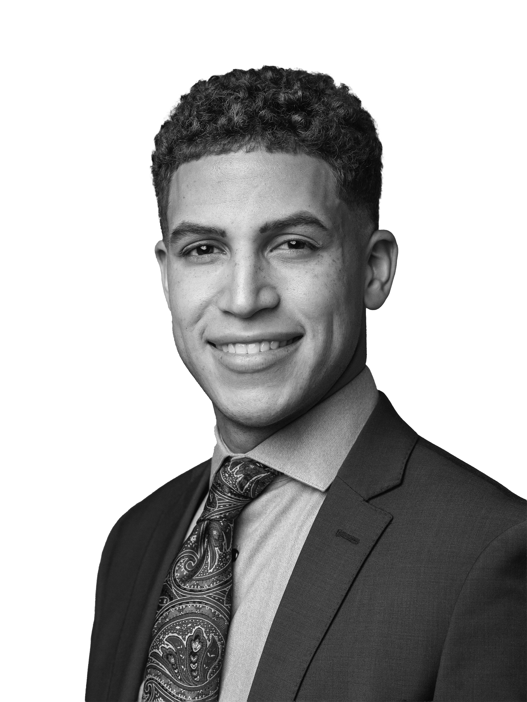 Black and white professional headshot of a young man wearing a suit, tie, and collared shirt, smiling at the camera.
