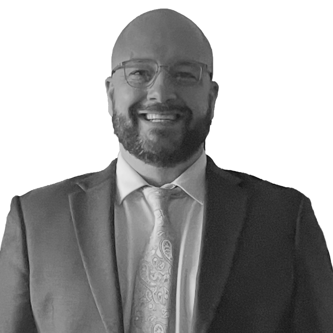 Black and white photo of a smiling man wearing glasses, a suit, a collared shirt, and a patterned tie.