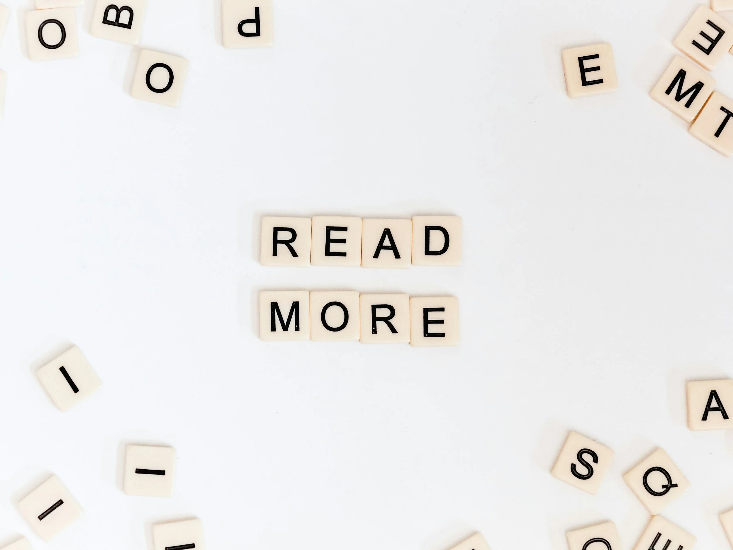Scrabble tiles on a white background spelling out "READ MORE" with scattered letter tiles around.