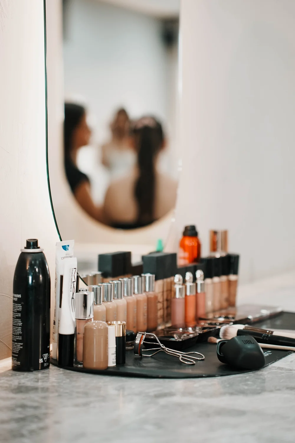 Foundations, brushes and hairspray laid out at a makeup station in front of a mirror