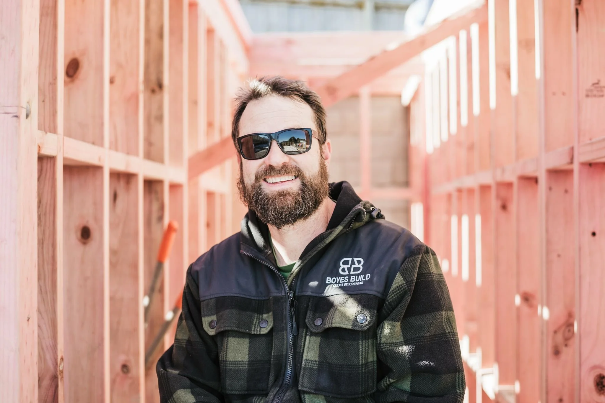 Man with sunglasses smiling at construction site with wooden framing.