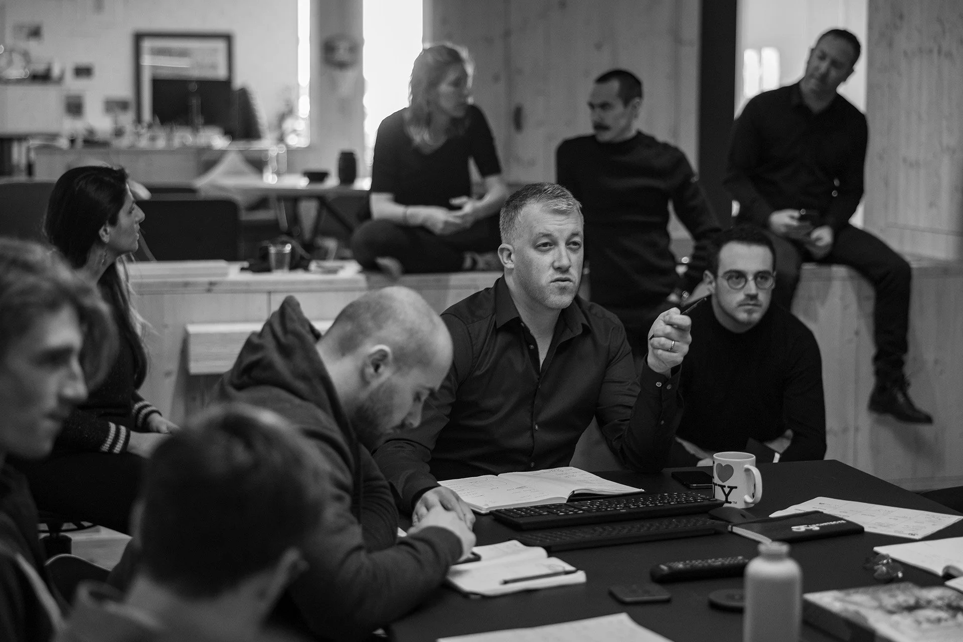 Groupe de personnes lors d'une réunion ou discussion dans une salle de conférence, en noir et blanc.