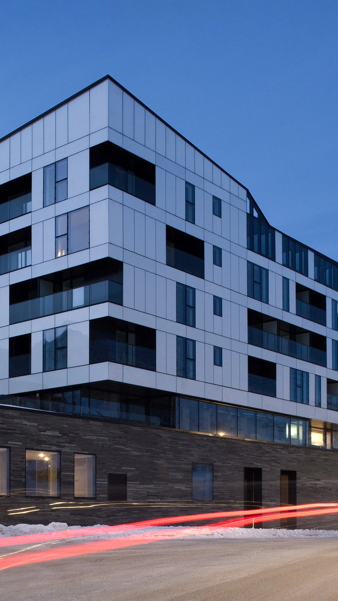 Un bâtiment moderne en hauteur avec des fenêtres en verre et un ciel bleu en arrière-plan, photographie prise au crépuscule.