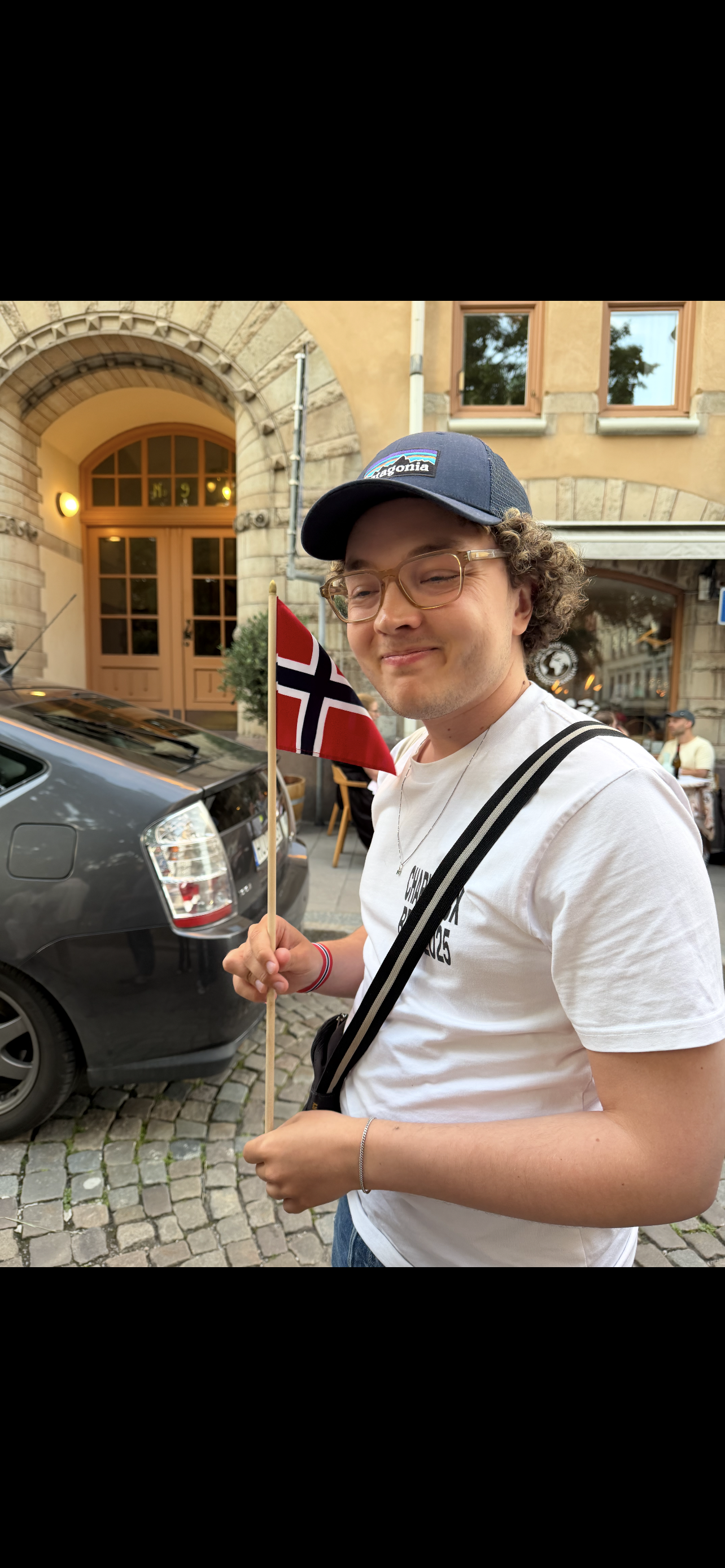 A young man with curly hair and glasses holding a Norwegian flag. An intern at the ICT4COP Center researching community-based policing and human security solutions.