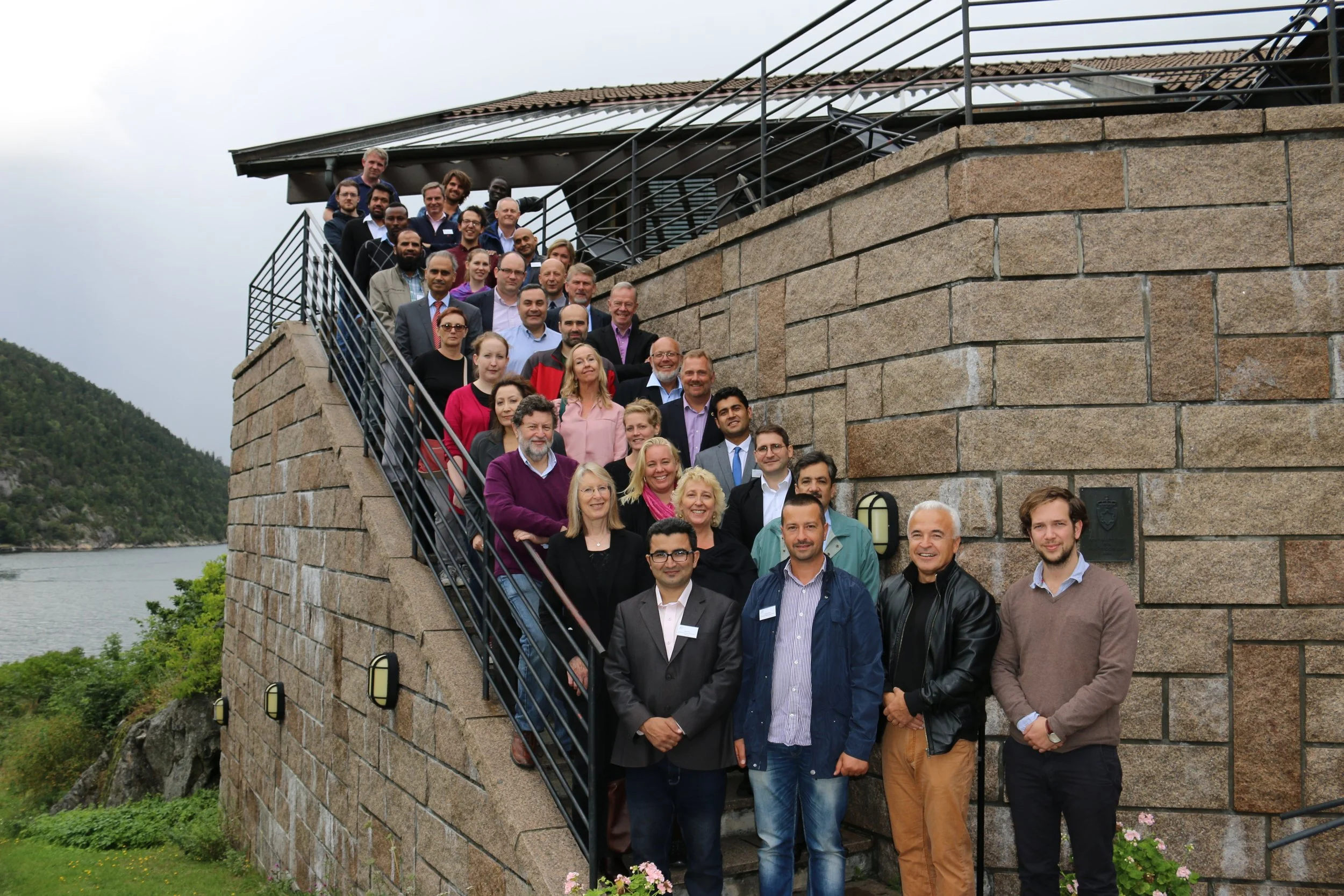 Group of ICT4COP researchers standing on a stone staircase outside, with a lake and greenery in the background, during cloudy weather.
