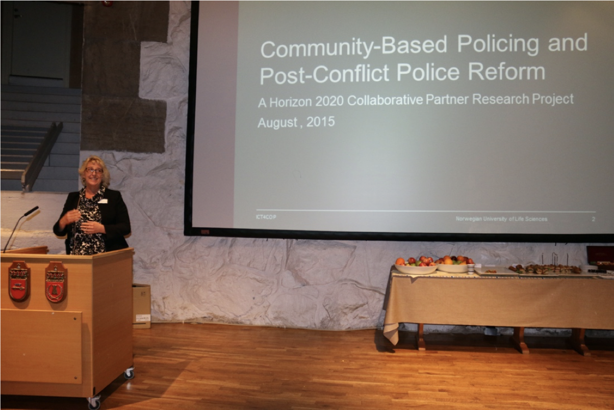 Professor Ingrid Nyborg stands at a podium with a presentation slide behind her, discussing community-based policing and post-conflict police reform at a conference or seminar.