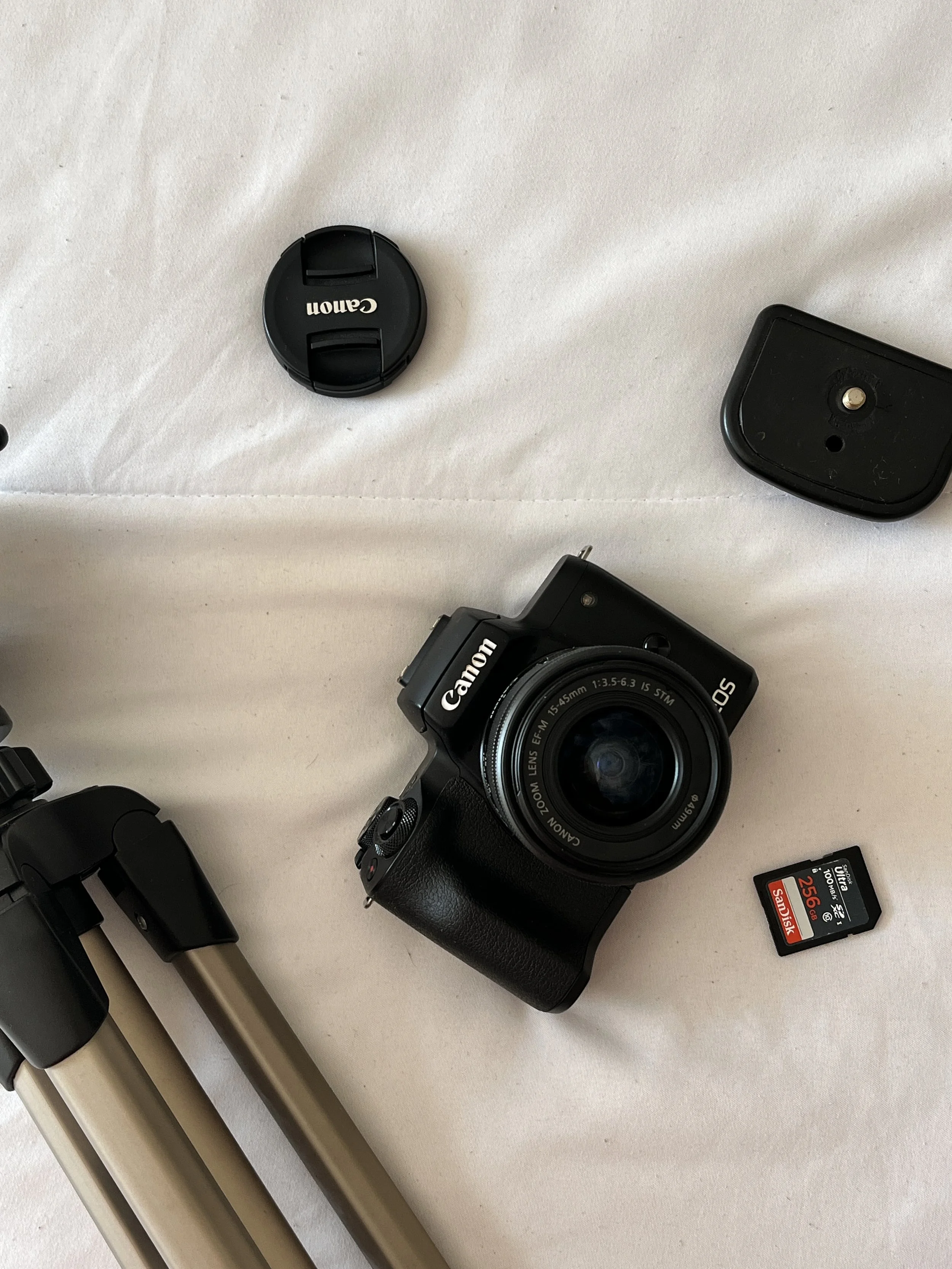 A camera, a canon lens cap, a tripod, a memory card, and camera accessories on a white surface.