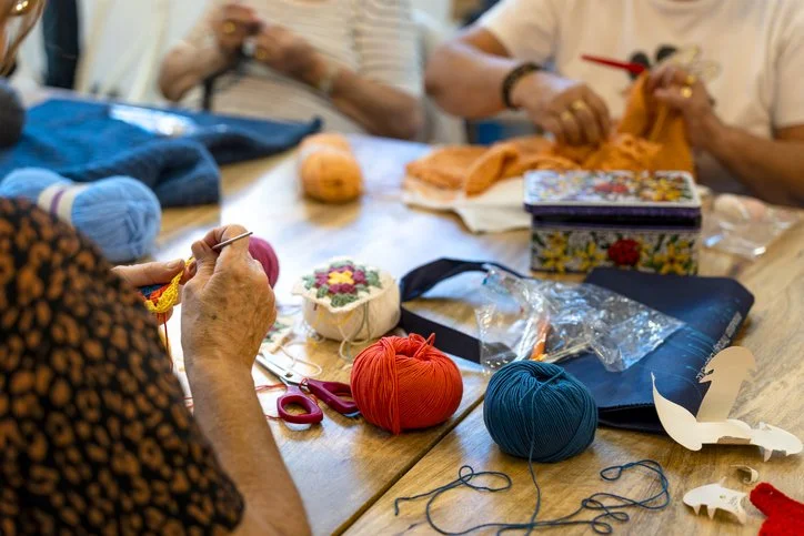 People crocheting and knitting with colorful yarn on a table.