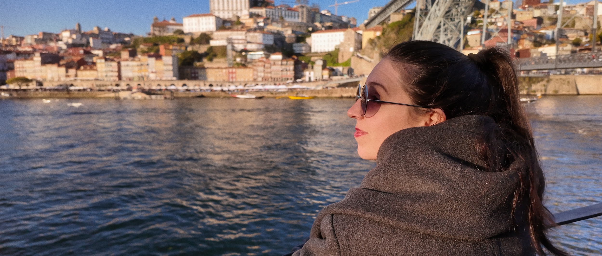 Woman in sunglasses enjoying river view with a cityscape in the background.