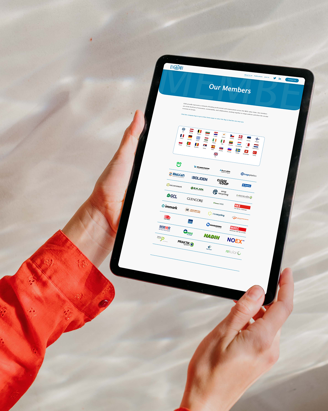 Person holding a tablet displaying a webpage with a header titled 'Our Members' featuring logos of various companies and a list of flags representing countries.