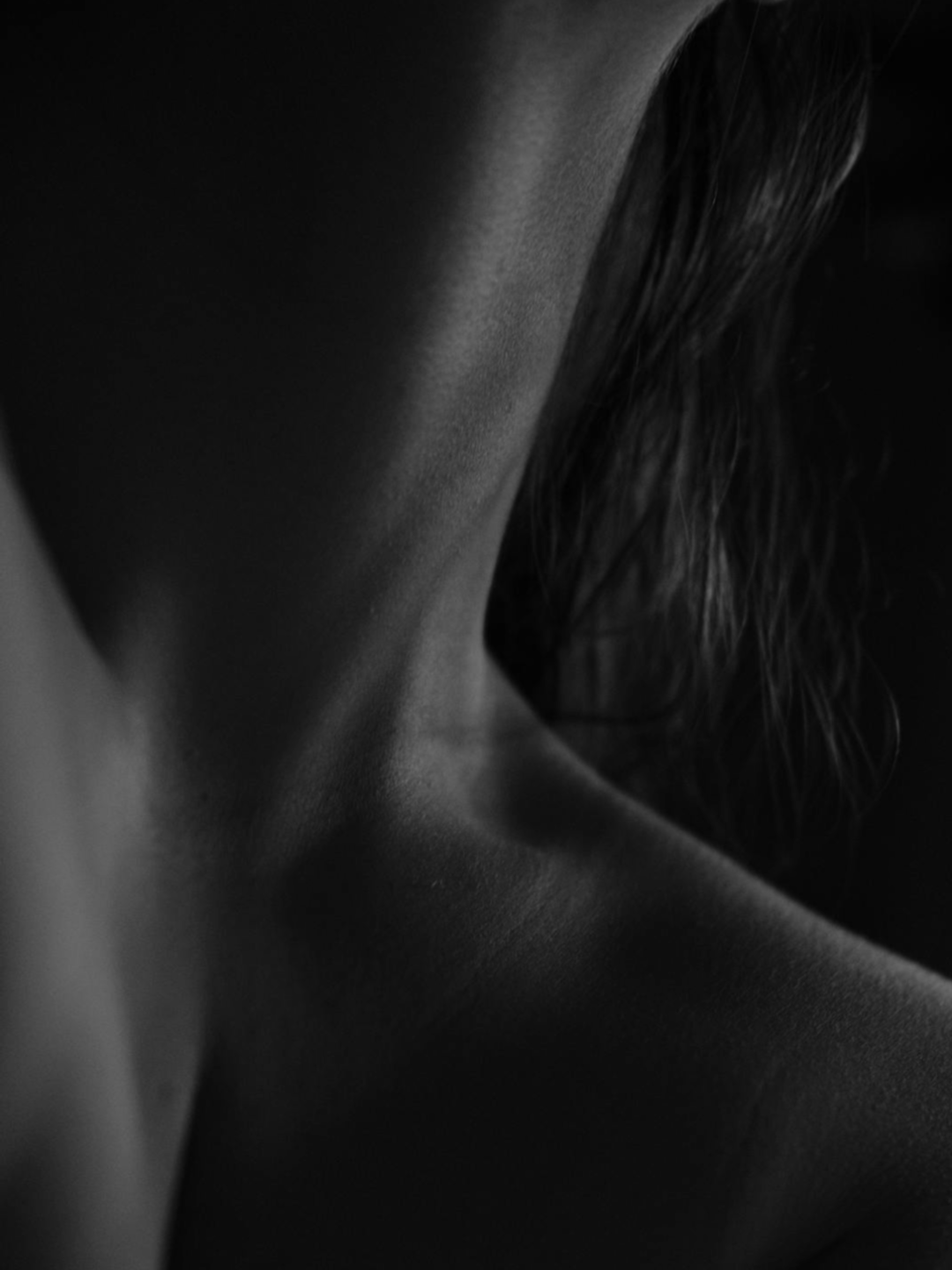 Close-up black-and-white photo of a person's neck, shoulder, and hair, showing smooth skin and textured hair.