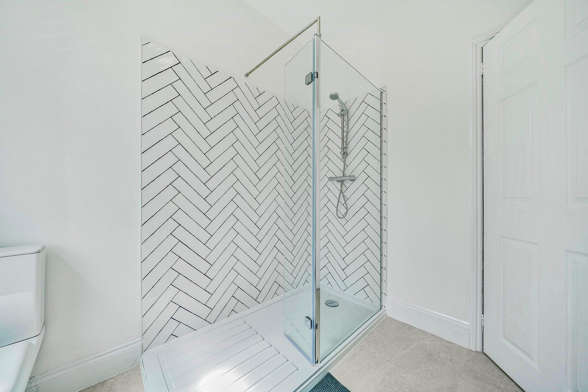 Modern bathroom with herringbone tiled shower, glass door, and white walls.
