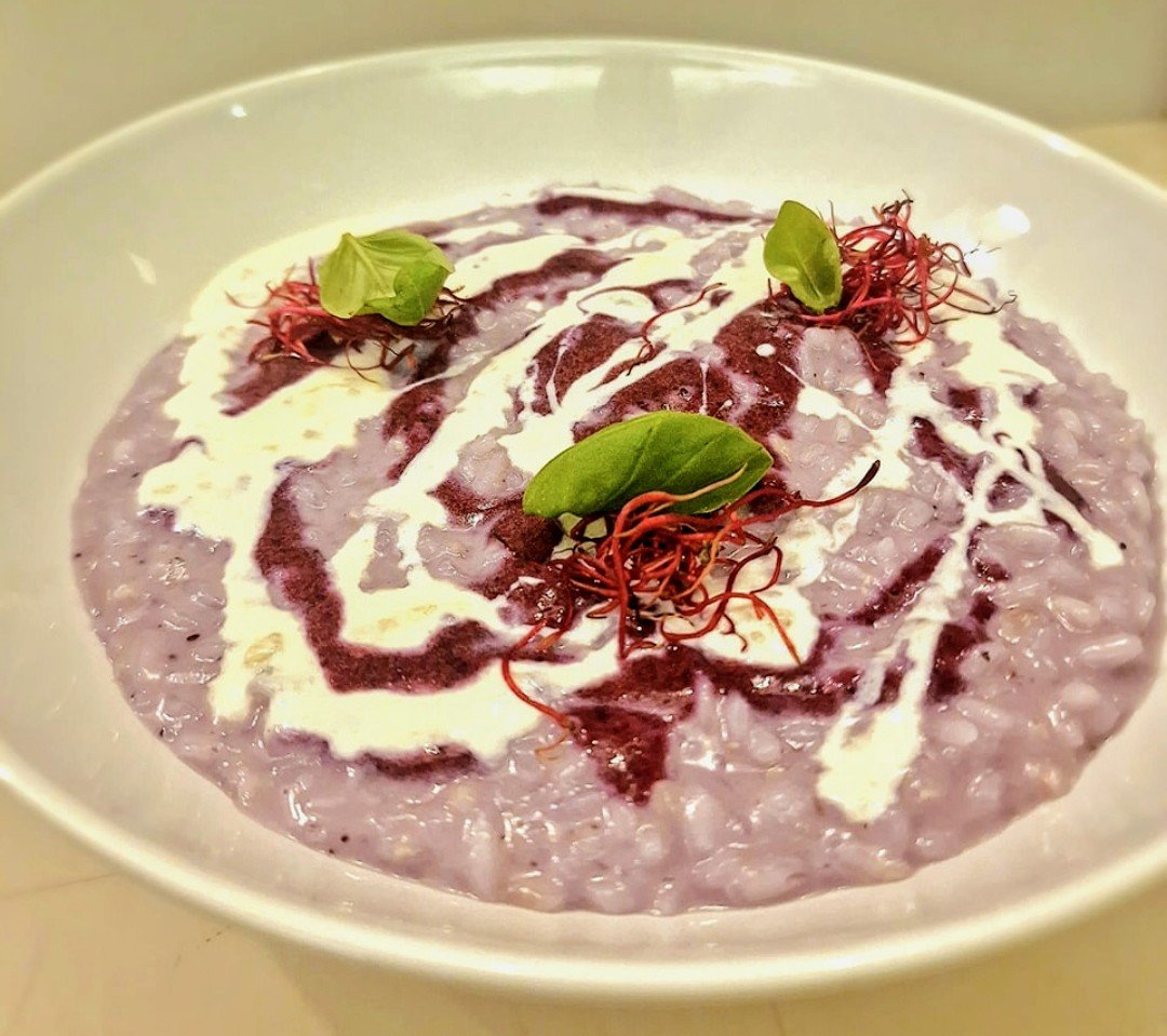 Risotto cremoso viola con salsa bianca, guarnito con erbe e fili di peperoncino in una ciotola bianca.