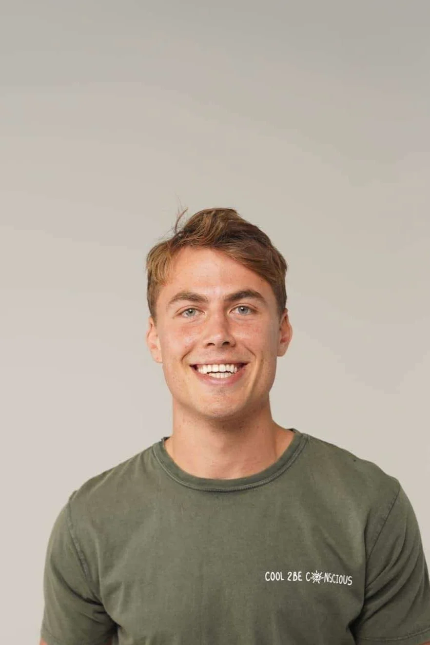 A person smiling and wearing a green shirt with the text 'Cool 2Be Conscious'